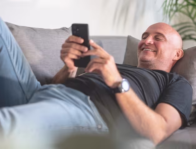 łysy uśmiechnięty facet leży na kanapie z komórką