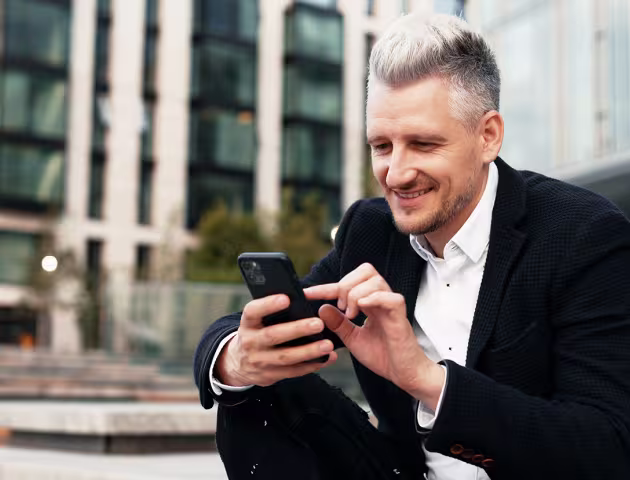 Mężczyzna w garniturze z telefonem siedzi przed biurowcem