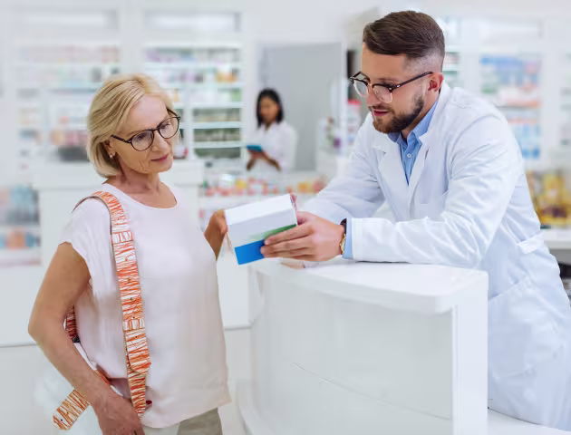 farmaceuta tłumaczy coś starszej pacjentce z lekiem w ręku