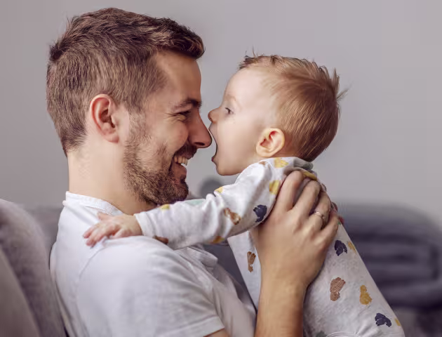 Tata z małym dzieckiem, trzyma je w ramionach i patrzą na siebie