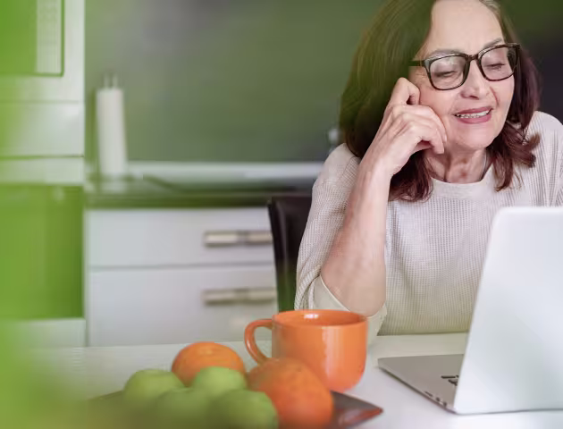 Kobieta ok 60ki przed laptopem, obok niej taca z pomarańczami