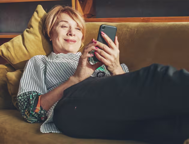Ruda 50latka na kanapie z telefonem
