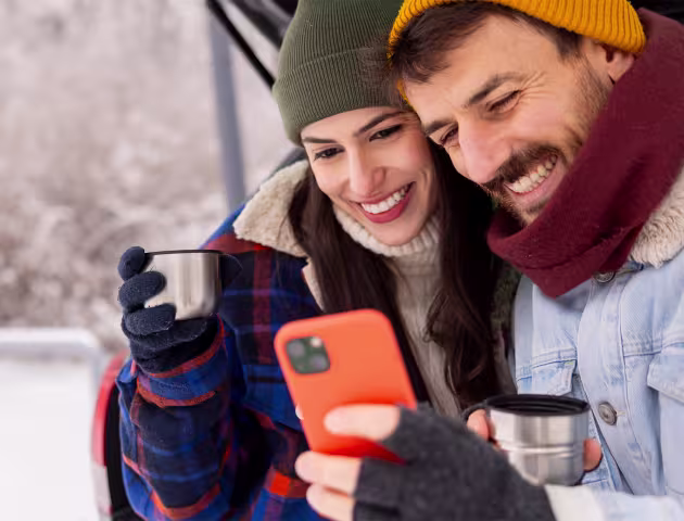 Usmiechnieta para patrzy na telefon, w tle zimowy krajobraz
