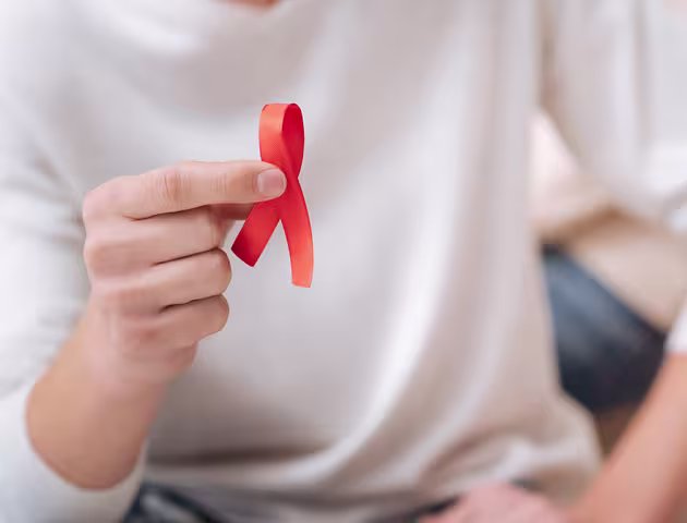 ręka trzymająca czerwoną wstążkę symbol AIDS