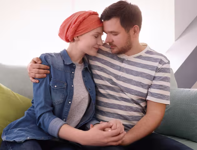 Młody mężczyzna i kobieta z chustką na głowie siedzą przytuleni na kanapie