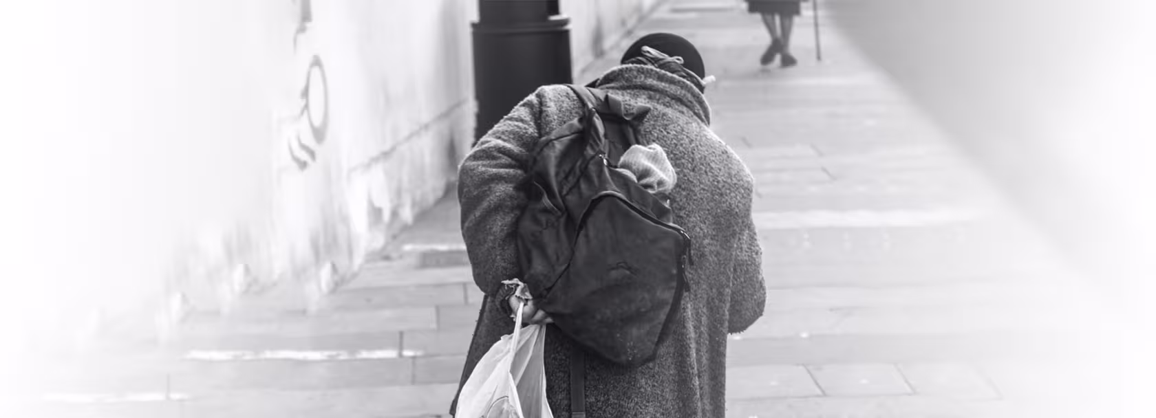 Bezdomna osoba z plecakiem i reklamówką, od tyłu, wchodząca po schodach
