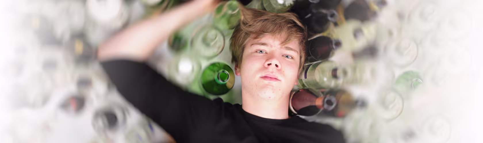 Nastolatek leży na podłodze, a dookoła niego stoją puste butelki po alkoholu.