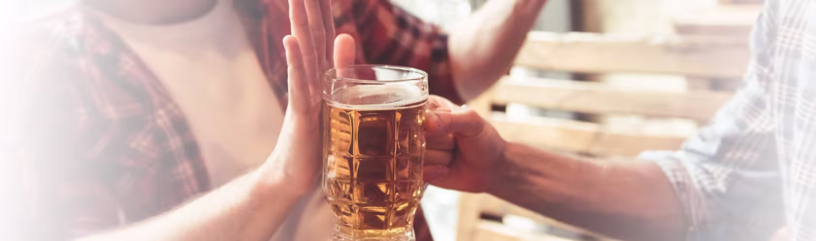 Mężczyzna podaje kufel z piwem koledze, ten odmawia dłonią blokując kufel.