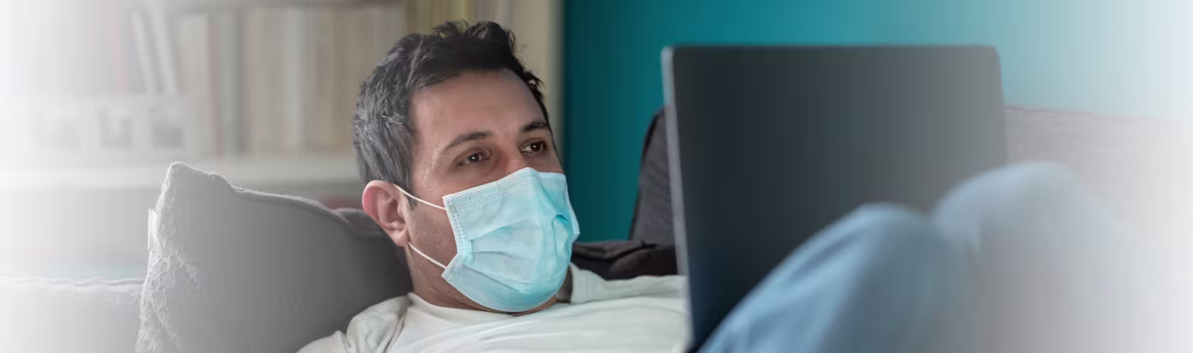 Mężczyna leży na kanapie z laptopem na kolanach i umawia się na test covid przez internet.