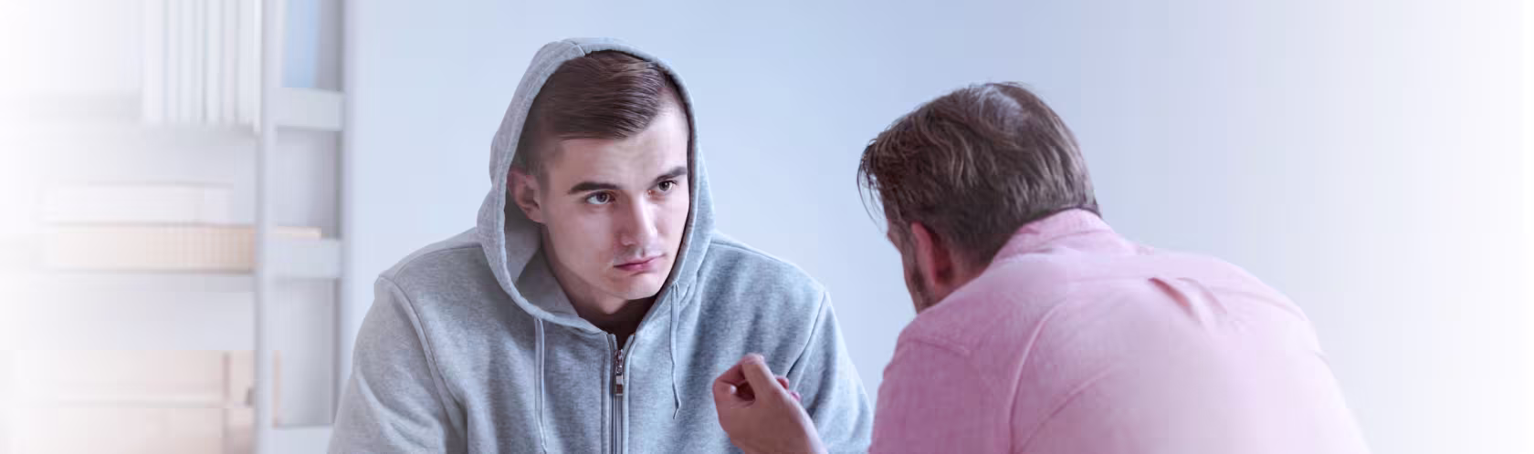 Młody chłopak siedzi i rozmawia z terapeutą. Ma na sobie dres, a na głowie kaptur.