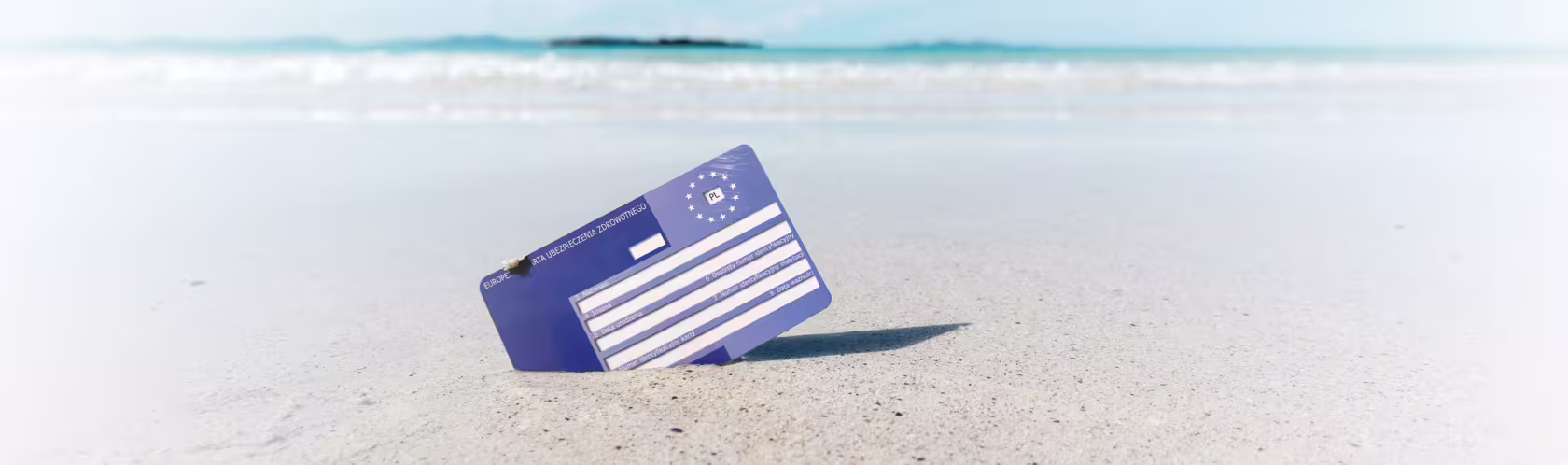 Karta EKUZ wbita w piasek na plaży. W tle błękitne morze.