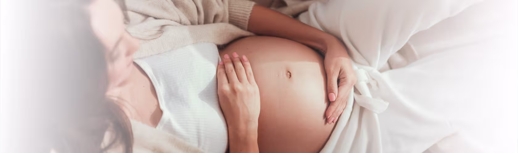 Leżąca kobieta w ciąży obejmuje brzuch dłońmi.