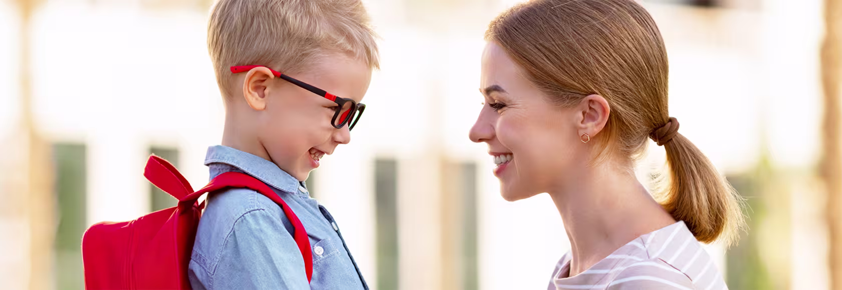 mama trzyma dziecko za obie ręce, kucając, chłopiec w okularkach śmieje się