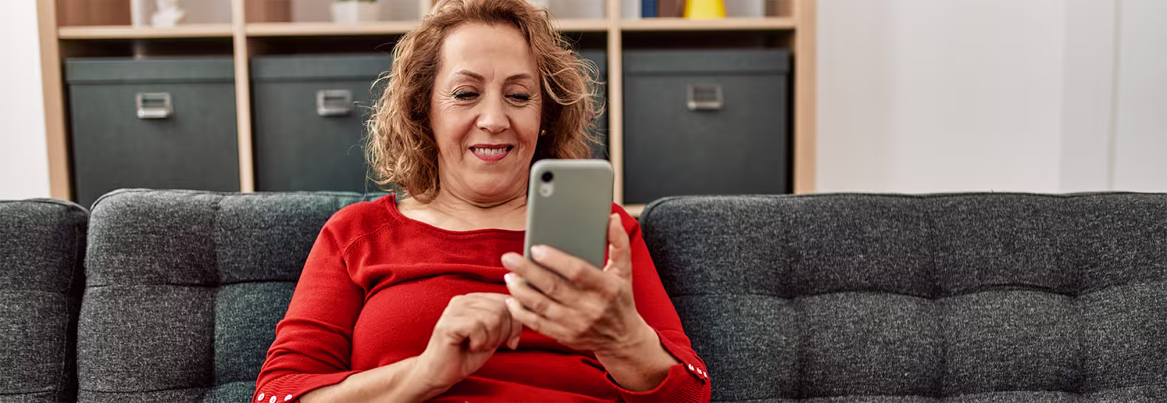 pani ok.40 siedzi na kanapie i z uśmiechem patrzy w telefon