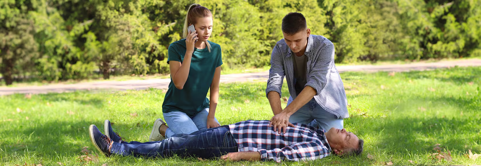 park, poszkodowany leży, dziewczyna dzwoni, chłopak robi masaż serca