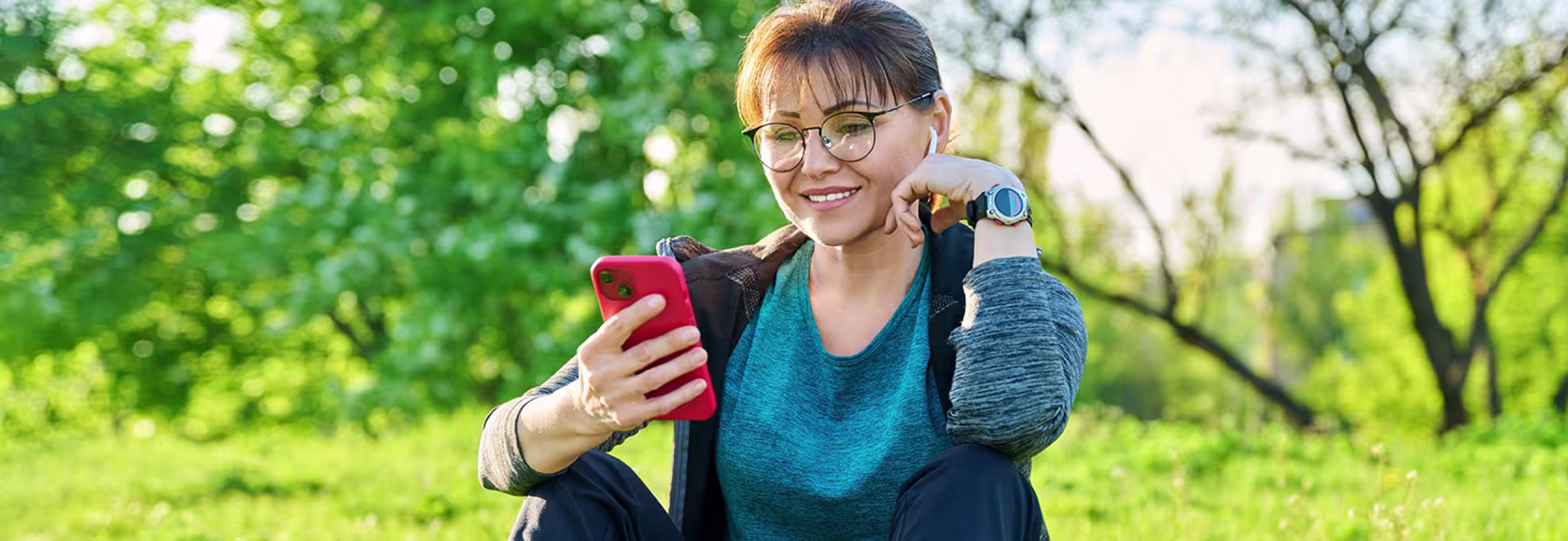 Pani siedząca na trawie z uśmiechem patrzy na telefon