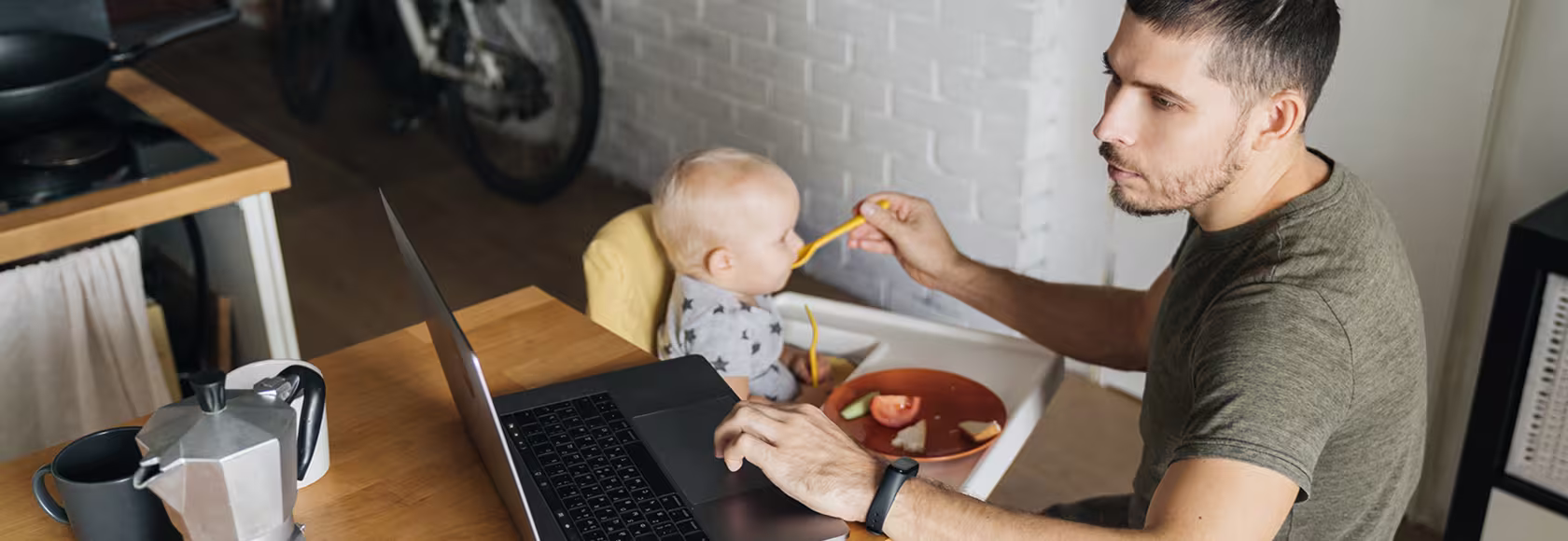 ojciec karmi dziecko łyżeczką i patrzy w laptop