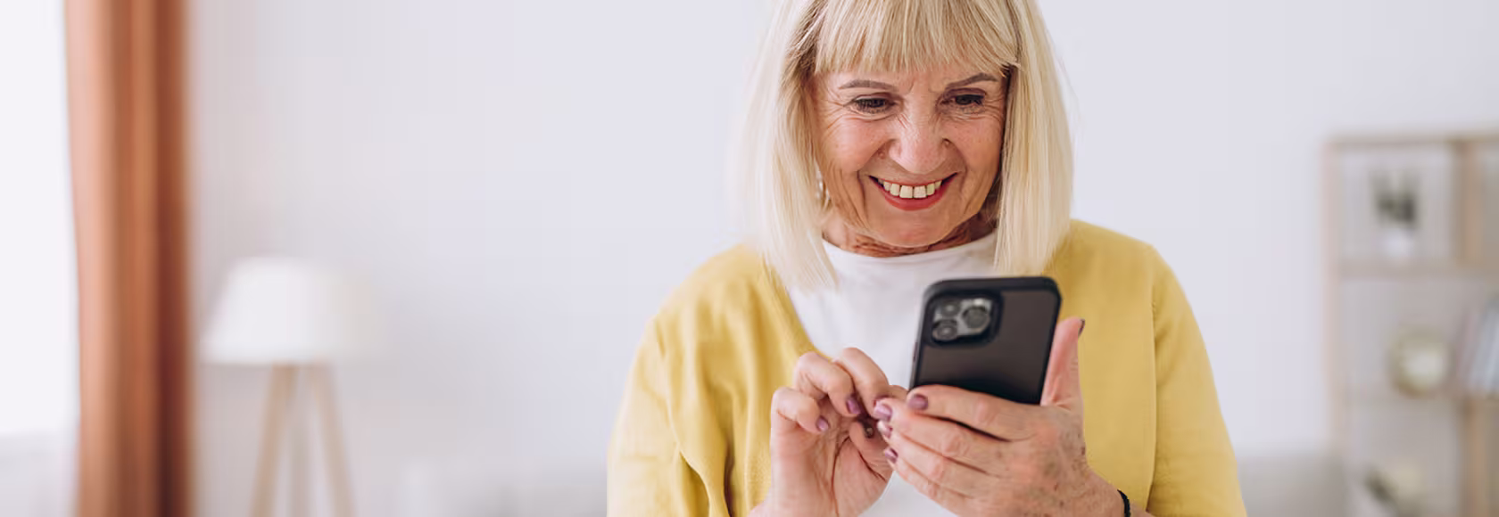 Seniorka z komorka w domu, w rozpiętym swetrze