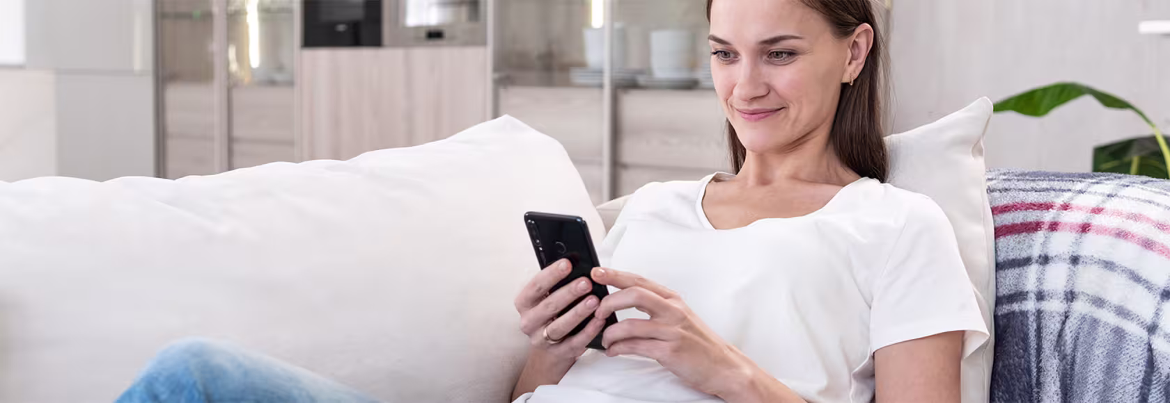Młoda kobieta lezy na kanapie i patrzy na ekran komórki. którą a w ręku