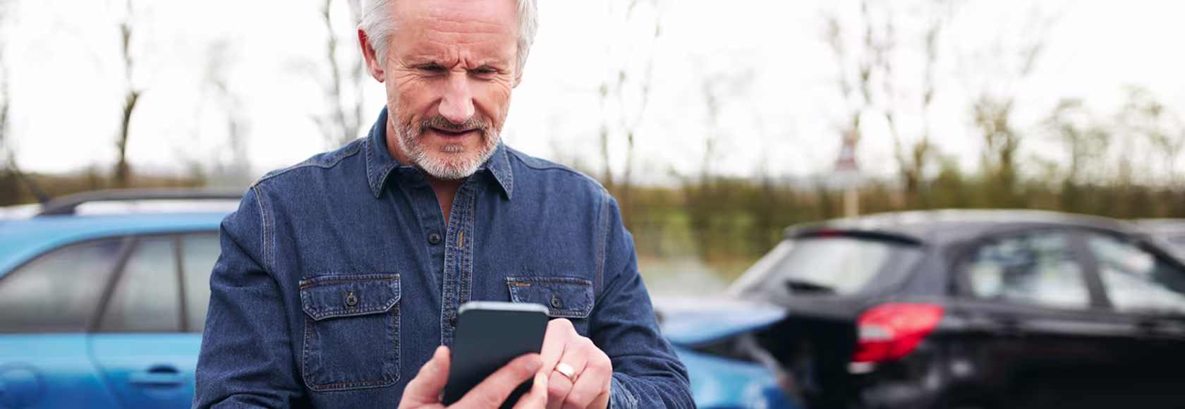 w tle zderzenie 2 aut mężczyzna z siwą bródką patrzy na telefon