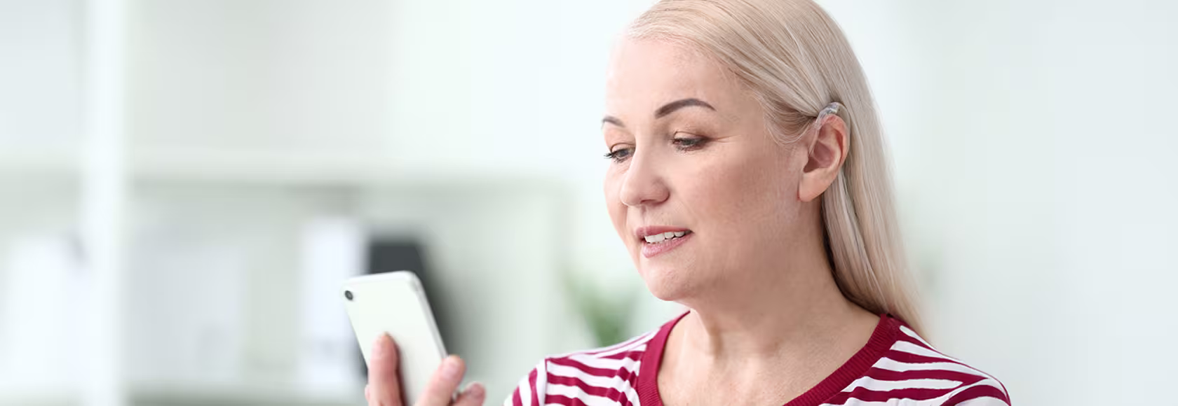 Blondynka z aparatem słuchowym patrzy na telefon 