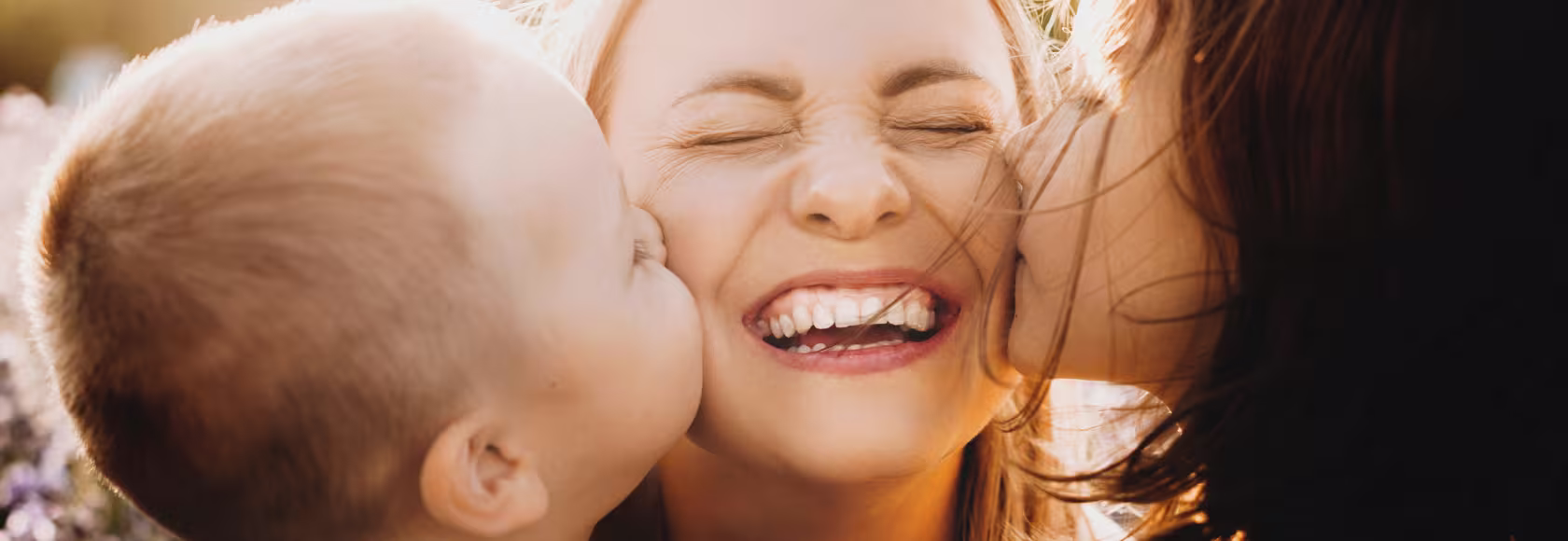 Dwoje dzieci całuje w policzki uśmiechniętą mamę