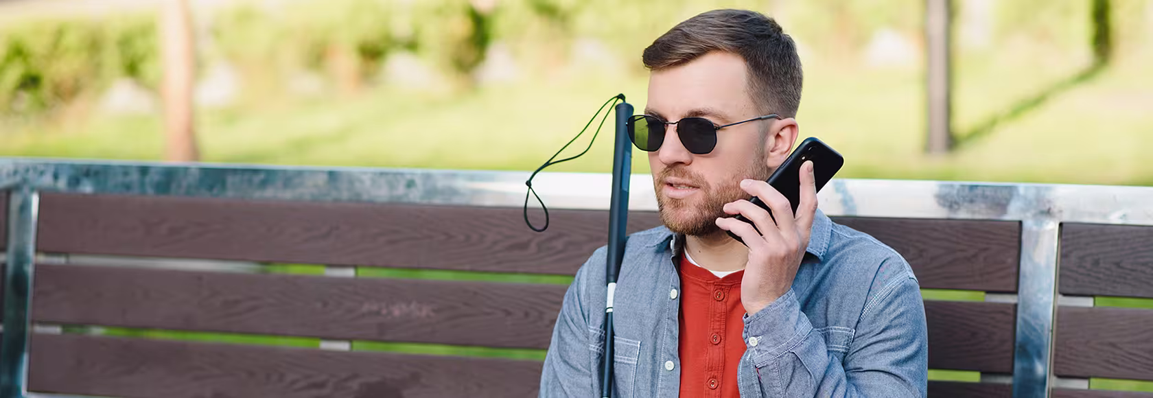 niewidomy mężczyzna z telefonem siedzi na ławce